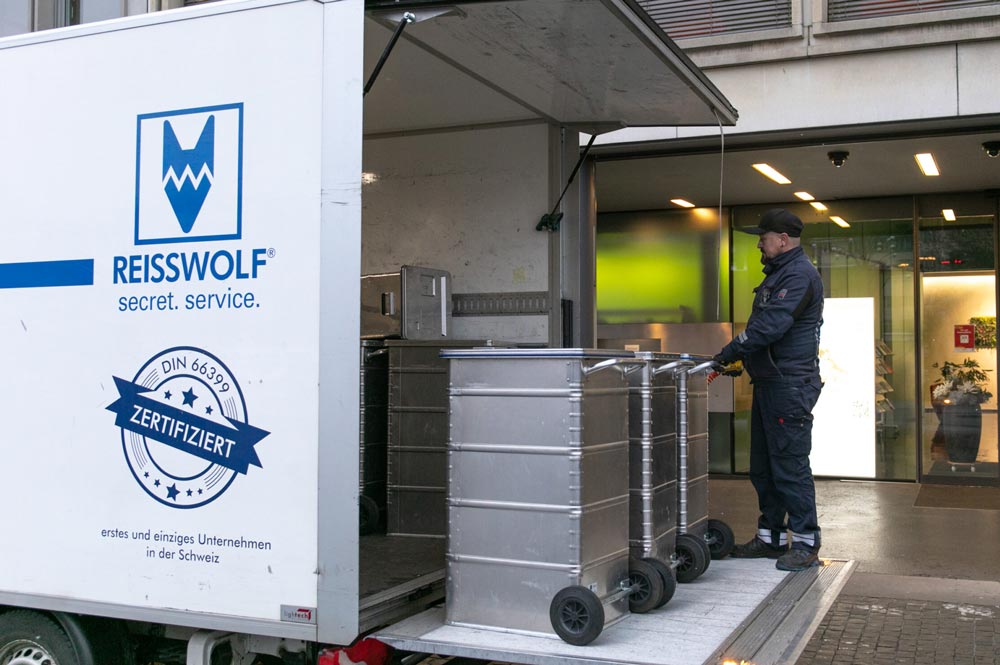 Sichere Abholung vertraulicher Dokumente durch REISSWOLF Schweiz: Ein Mitarbeiter verlädt verschlossene Sicherheitsbehälter in ein GPS-überwachtes Fahrzeug – konform mit dem revDSG und DIN 66399.